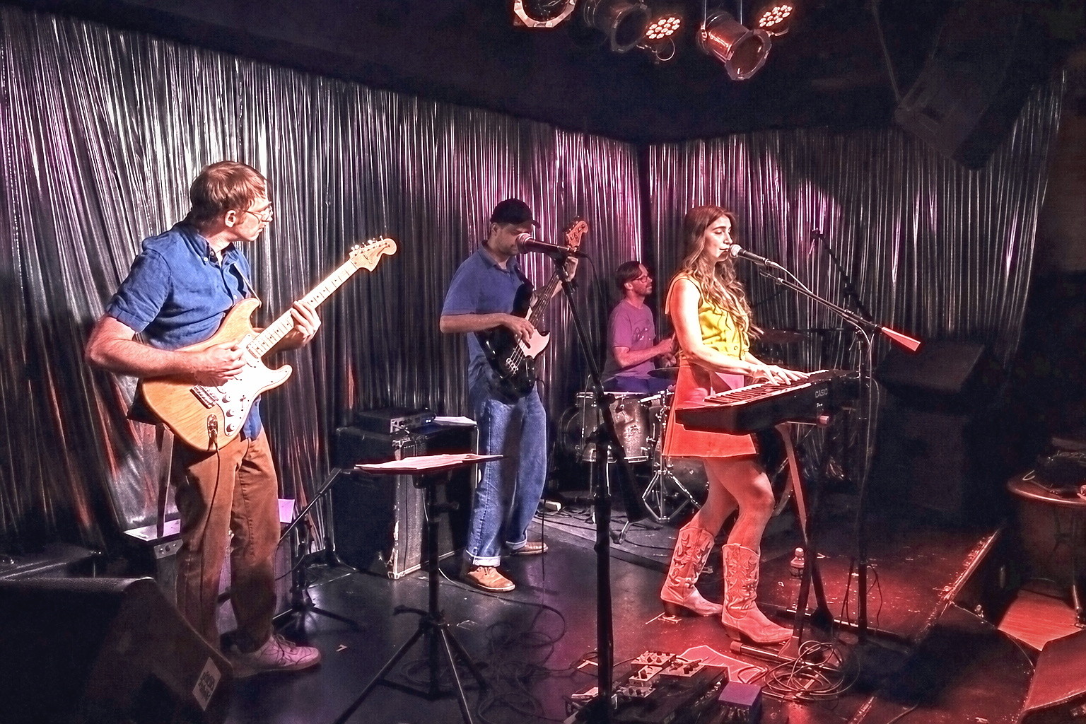 A four-piece band playing on a small stage in a near-empty room