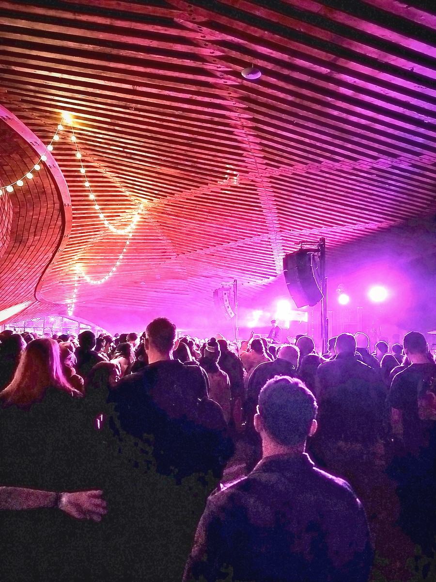 Crowd silhouetted under a slatted ceiling washed in pink light