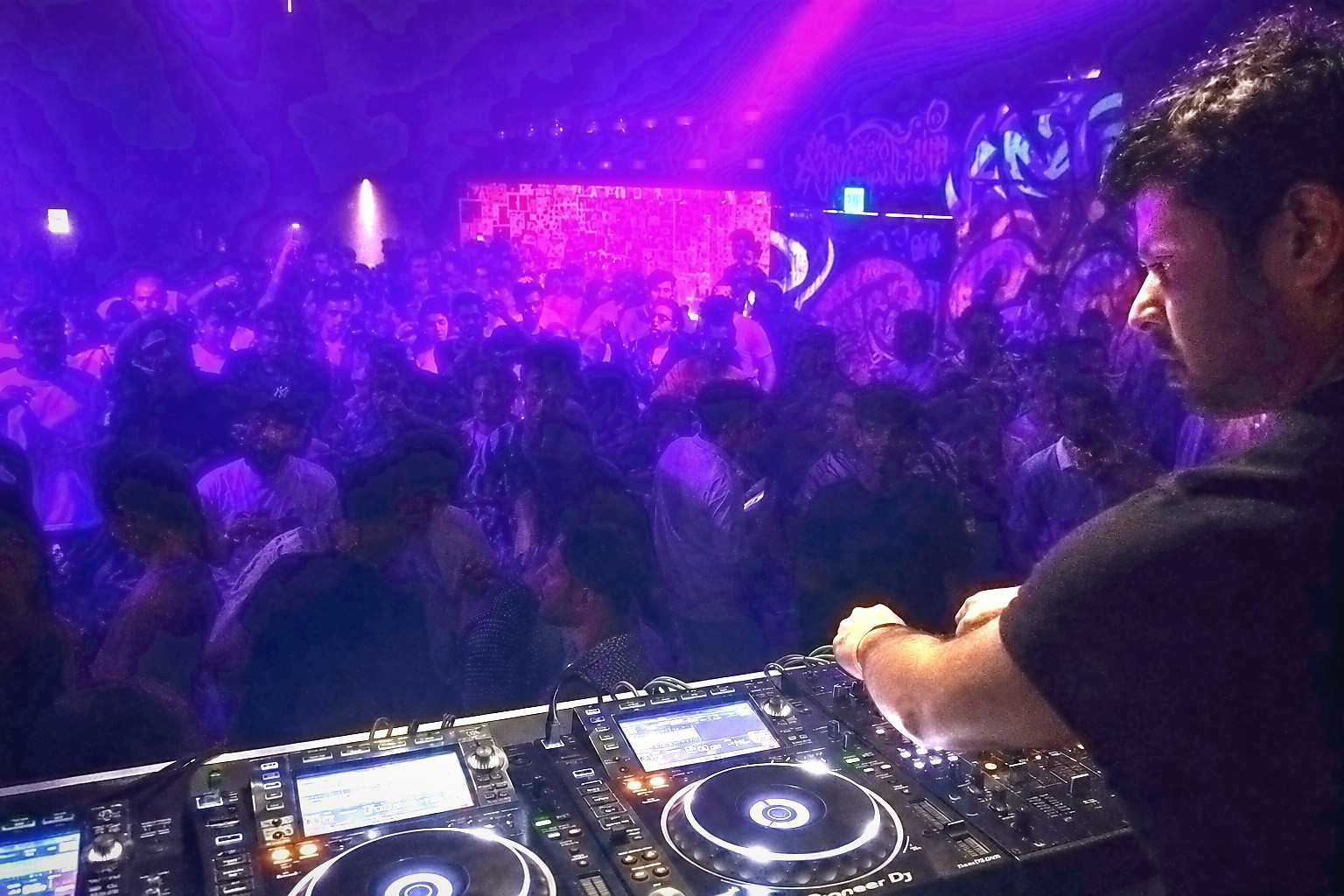 A DJ working CDJ decks with a crowded room behind