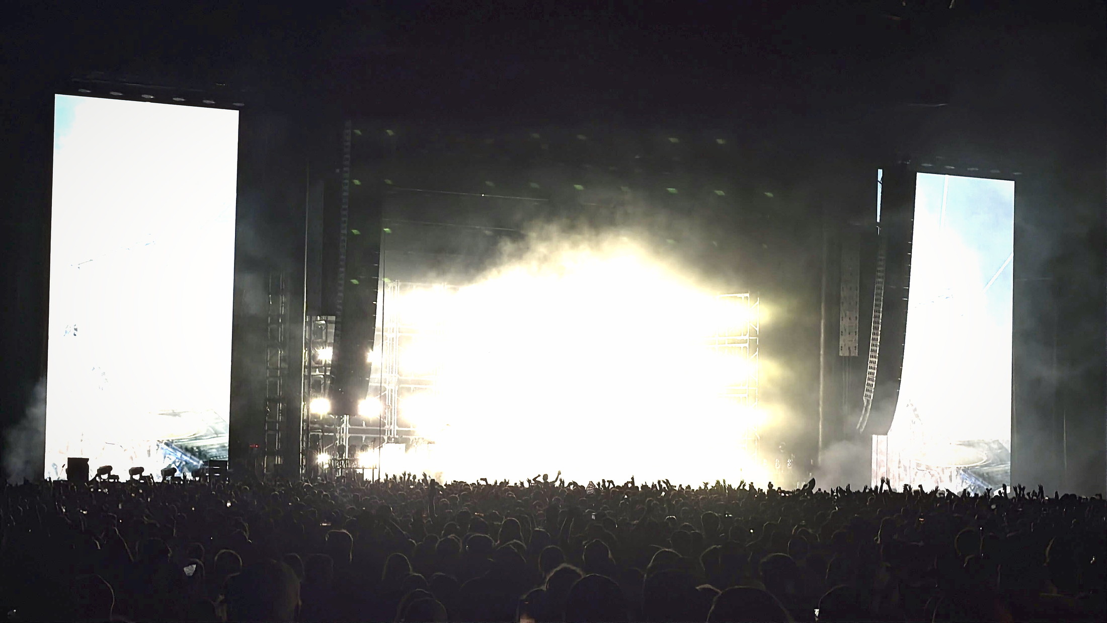 A vast crowd in silhouette before a stage engulfed in white light and smoke