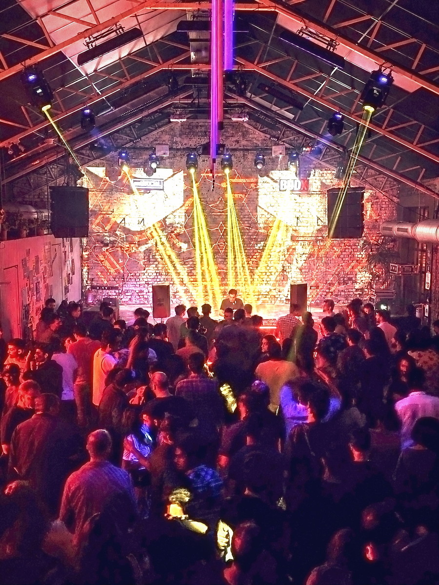 A warehouse venue with exposed trusses, lasers overhead and a full floor
